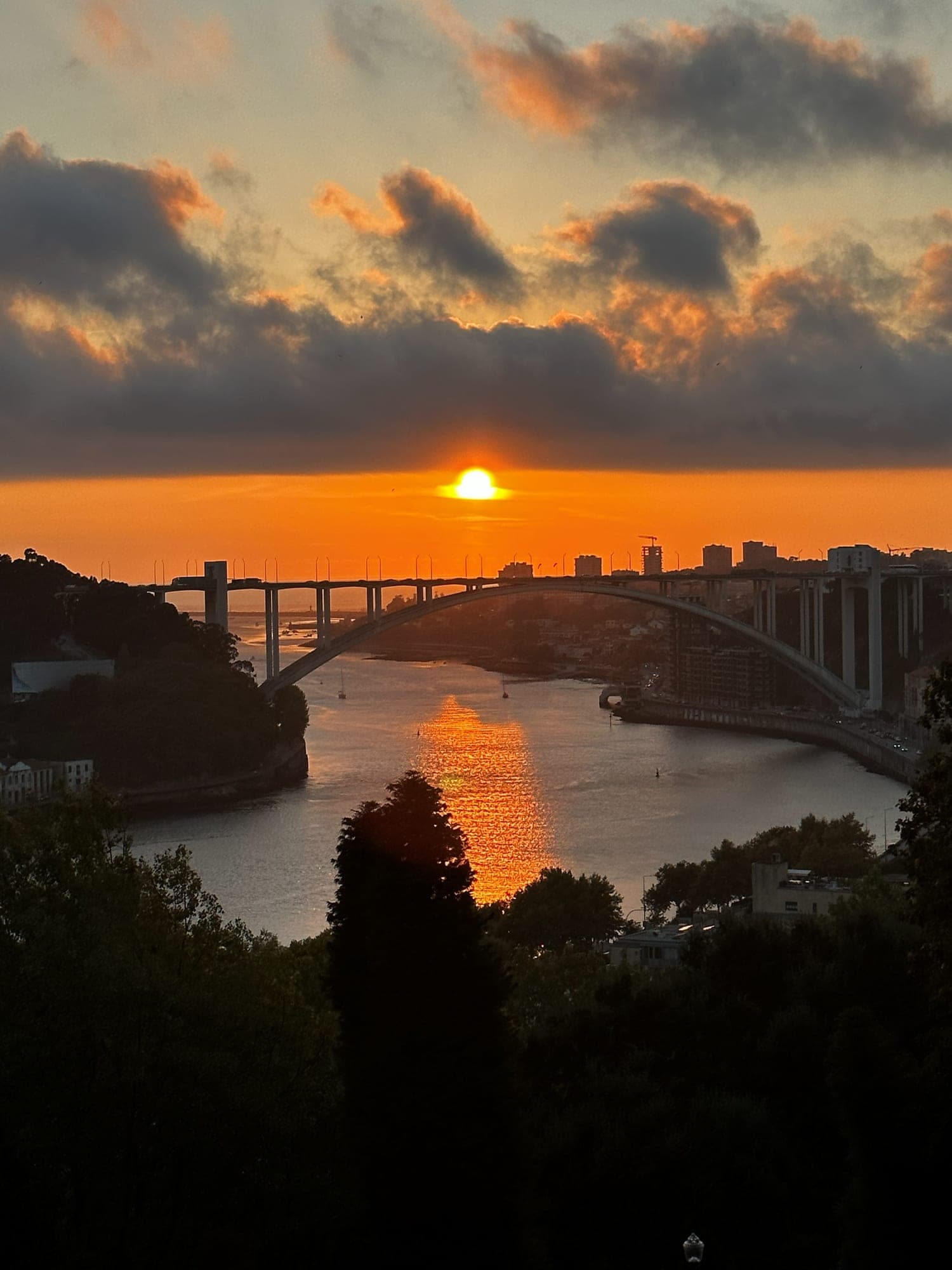 The sun setting over the Douro river in Porto, with the arch of the Arrábida Bridge across the water