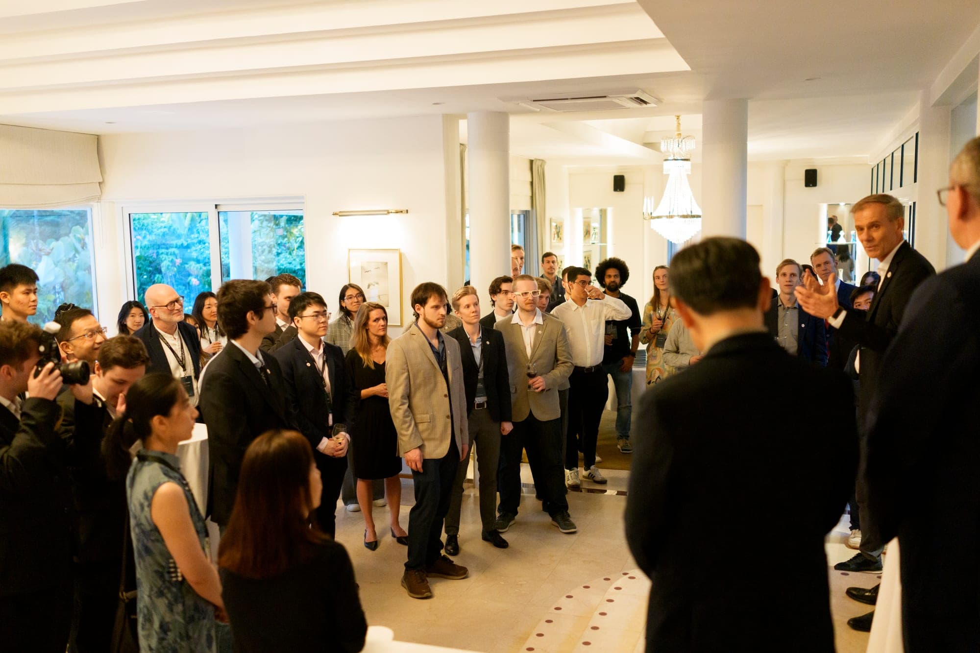 WASP students and guests standing in a white reception room listening to the Ambassador