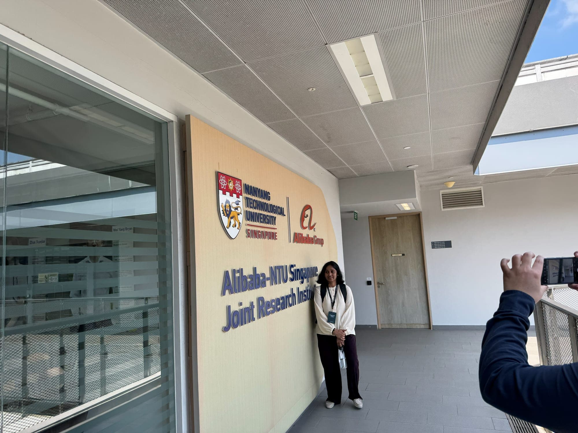 A WASP student posing by the Alibaba-NTU Singapore Joint Research Institute sign while another takes a photo