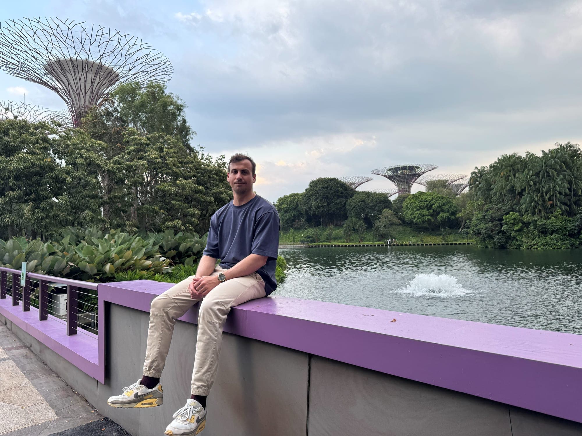 Dominik sitting by the lake at Gardens by the Bay with the Supertrees behind