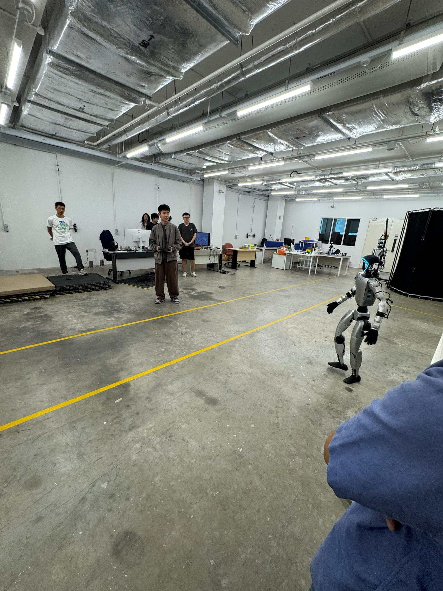 A small humanoid robot walking across a lab floor while researchers watch
