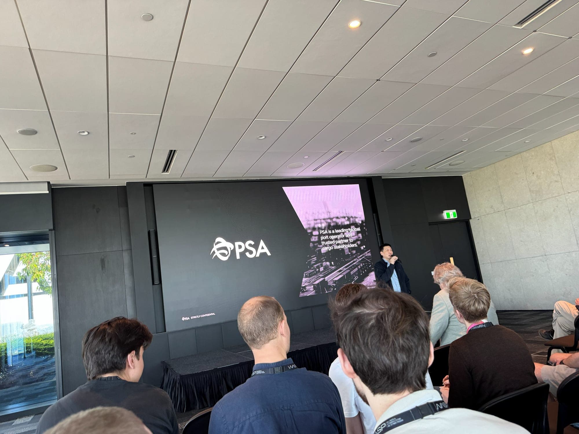 A speaker presenting next to a large PSA logo on a screen to a seated audience