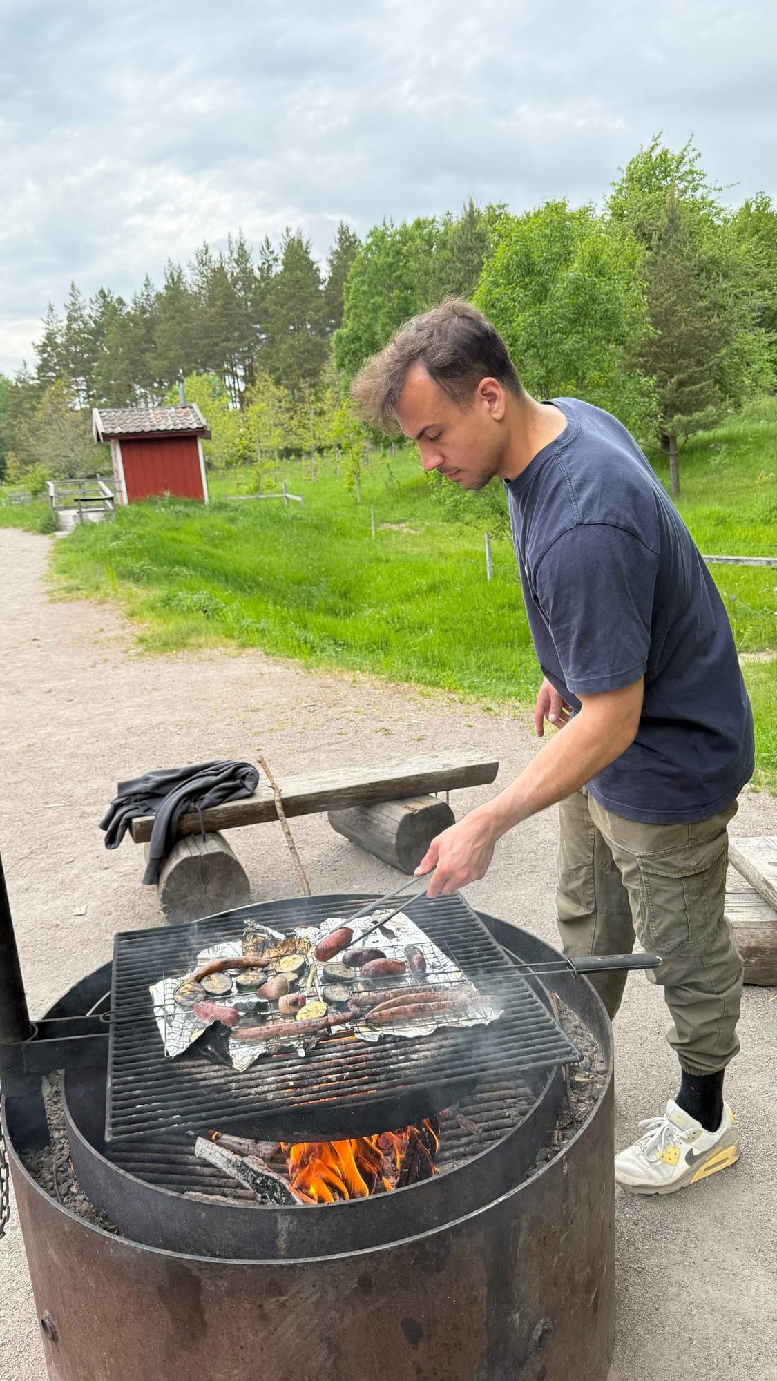 Dominik grilling sausages and vegetables over an outdoor fire pit in Sweden