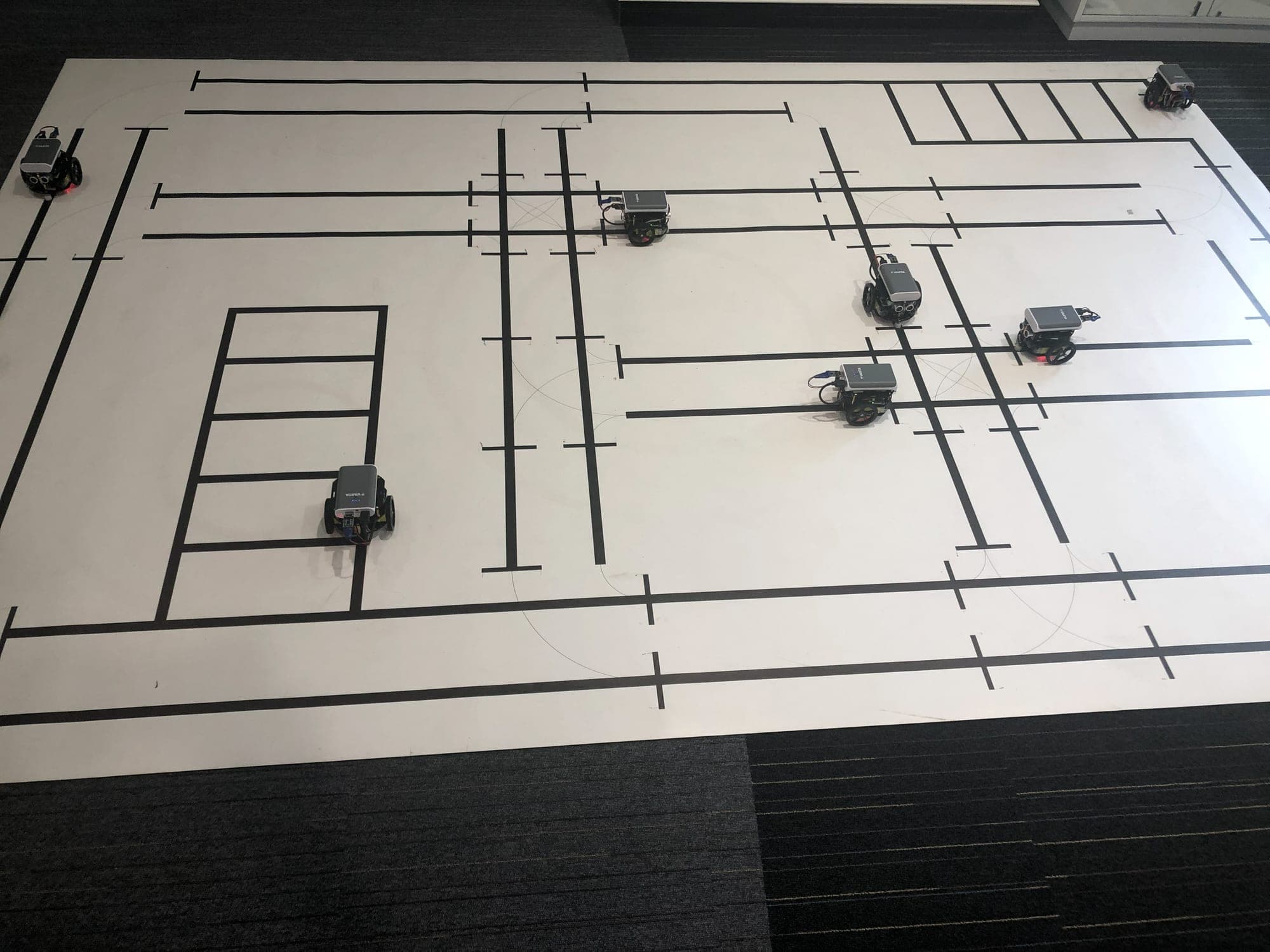 Several small autonomous robot cars on a test track printed with black lines on a large white mat