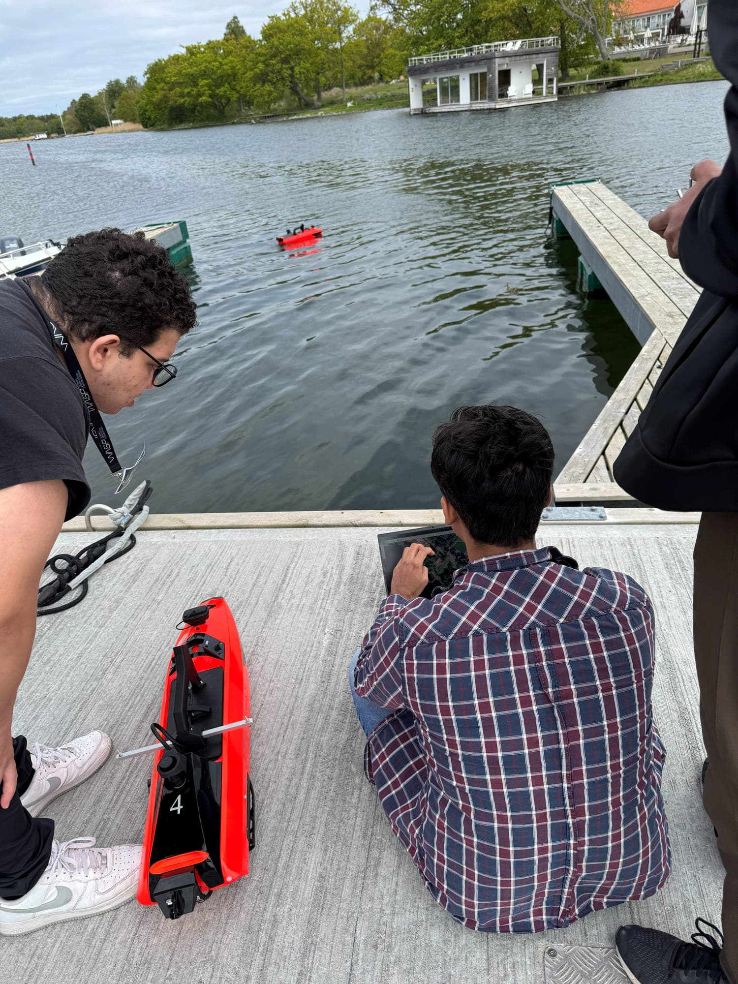 Researchers on a dock preparing a small red uncrewed surface vessel while a second one is already out on the water